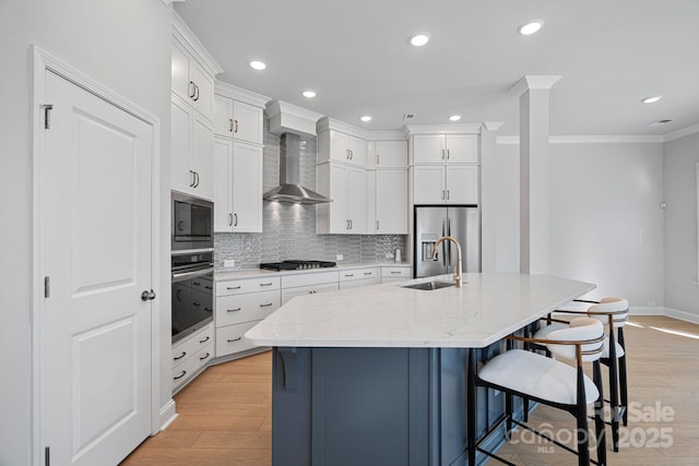 kitchen featuring a breakfast bar, light wood-style flooring, a sink, appliances with stainless steel finishes, and wall chimney exhaust hood