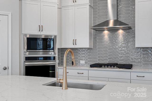 kitchen featuring a sink, stainless steel appliances, decorative backsplash, and wall chimney range hood