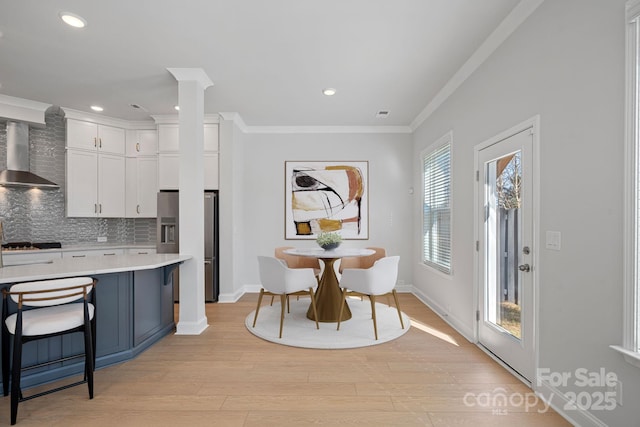 kitchen featuring stainless steel refrigerator with ice dispenser, backsplash, wall chimney exhaust hood, crown molding, and light countertops