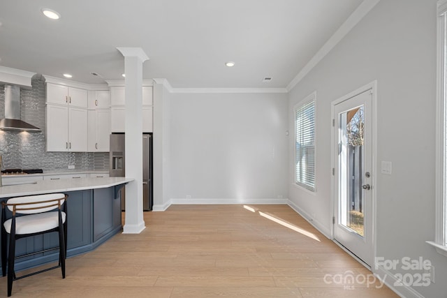 kitchen featuring tasteful backsplash, wall chimney range hood, light countertops, ornamental molding, and stainless steel fridge