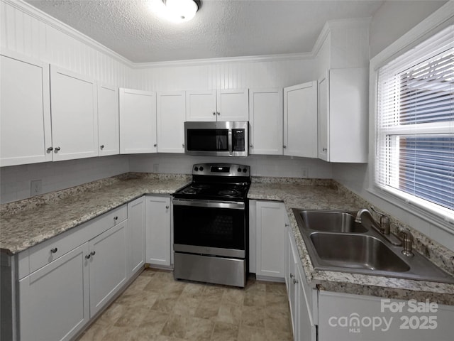 kitchen with a textured ceiling, white cabinets, appliances with stainless steel finishes, and a sink