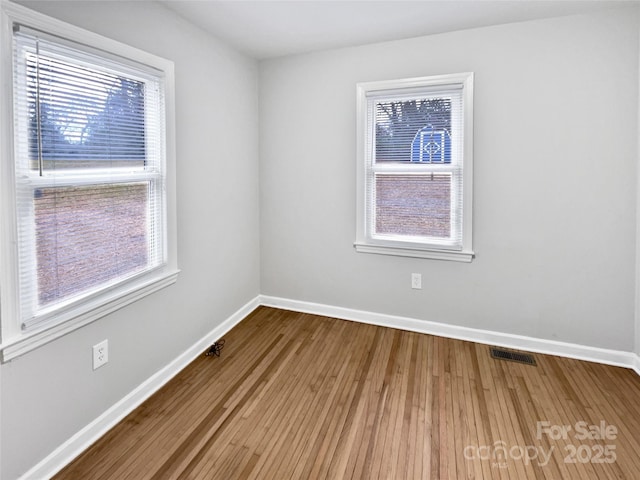 unfurnished room featuring wood finished floors, baseboards, and visible vents