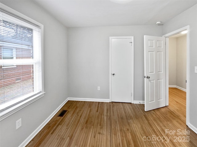 unfurnished bedroom featuring visible vents, wood-type flooring, multiple windows, and baseboards