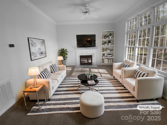 living area featuring visible vents, a ceiling fan, ornamental molding, and a high end fireplace