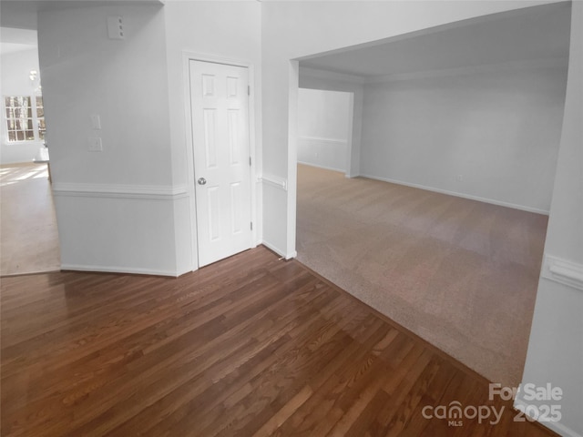 carpeted spare room featuring baseboards and wood finished floors