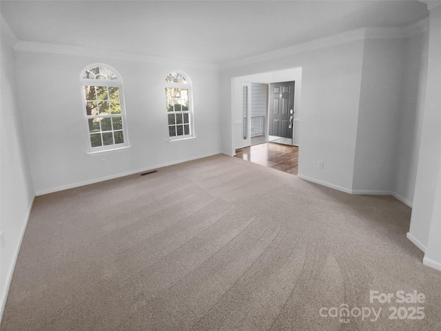 carpeted spare room featuring visible vents, baseboards, and ornamental molding