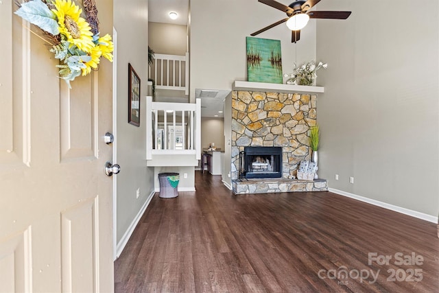 unfurnished living room with wood finished floors, baseboards, ceiling fan, a stone fireplace, and a towering ceiling