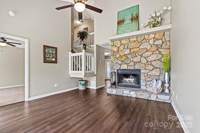 unfurnished living room with wood finished floors, a high ceiling, a fireplace, baseboards, and ceiling fan