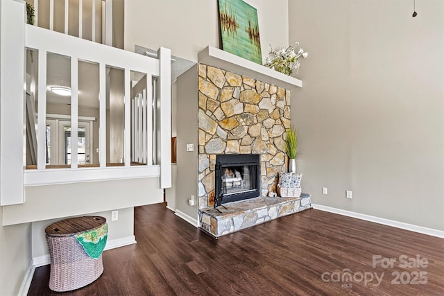 living area with a stone fireplace, a high ceiling, baseboards, and wood finished floors