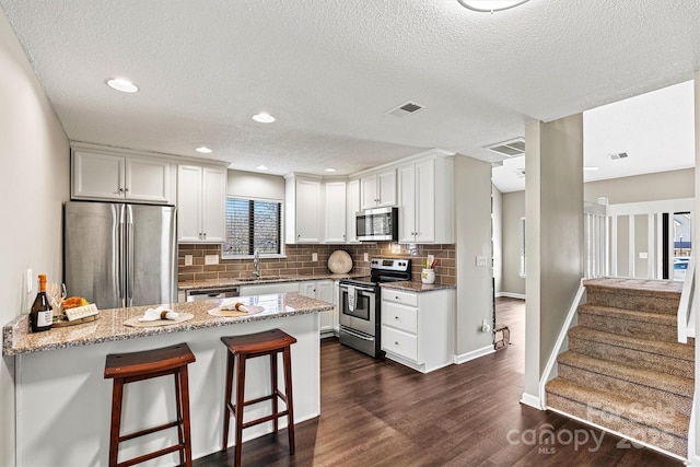 kitchen with a sink, light stone countertops, appliances with stainless steel finishes, a peninsula, and dark wood-style flooring