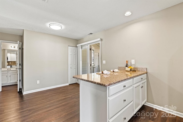 kitchen with baseboards, visible vents, dark wood finished floors, a peninsula, and white cabinetry