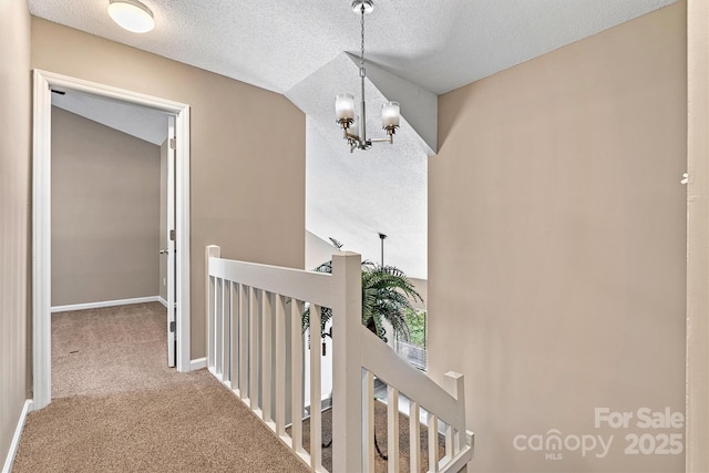 hall featuring baseboards, an upstairs landing, carpet flooring, a notable chandelier, and a textured ceiling