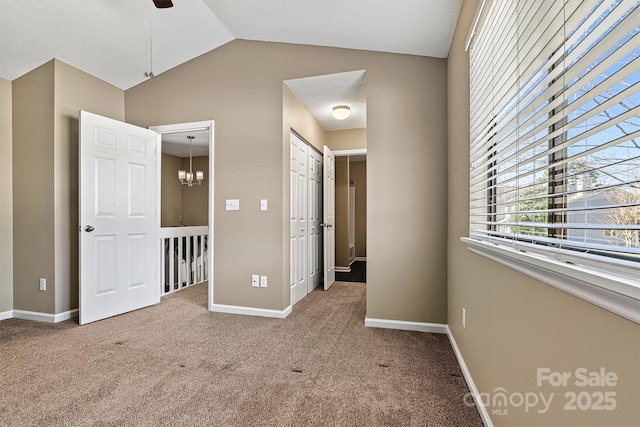 unfurnished bedroom featuring vaulted ceiling, a notable chandelier, carpet flooring, and baseboards