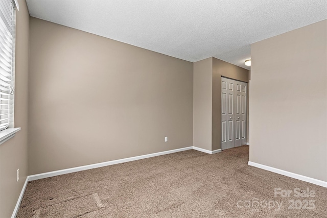 empty room with carpet flooring, baseboards, and a textured ceiling