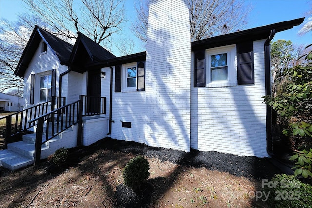 view of front of property featuring brick siding, crawl space, and a chimney