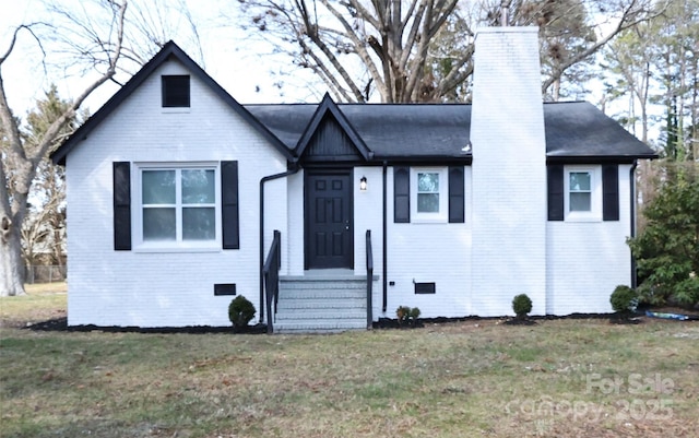 view of front of property with a front yard, a chimney, brick siding, and crawl space