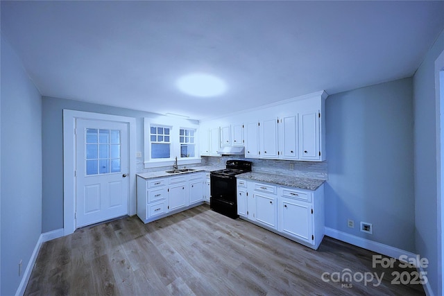 kitchen featuring under cabinet range hood, light wood-style floors, electric range, white cabinetry, and a sink