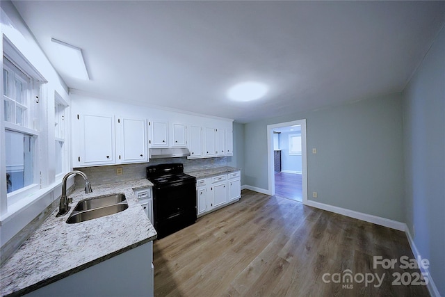 kitchen featuring light wood-style flooring, black electric range, under cabinet range hood, a sink, and white cabinetry