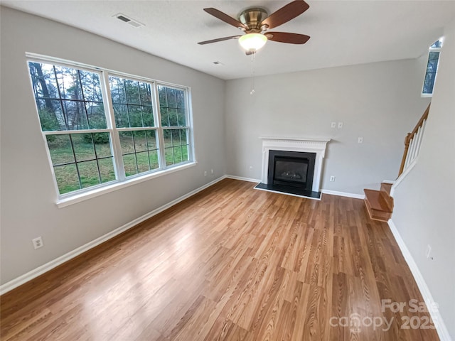 unfurnished living room with visible vents, a glass covered fireplace, wood finished floors, baseboards, and stairs