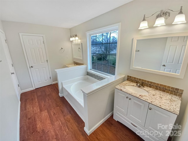 full bathroom with vanity, a garden tub, wood finished floors, and backsplash