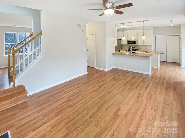 unfurnished living room featuring stairs, baseboards, light wood-type flooring, and ceiling fan