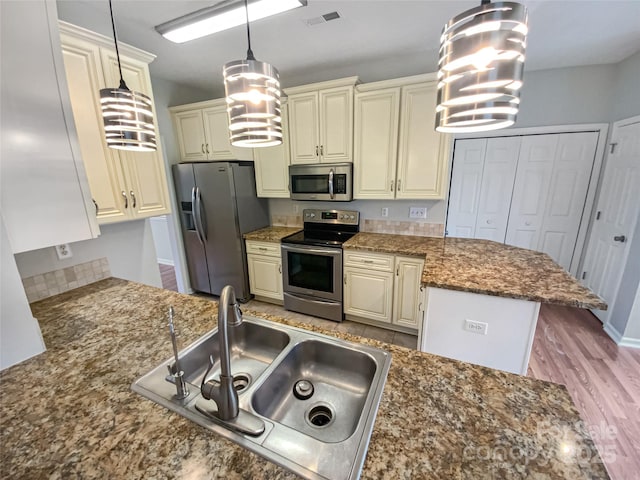 kitchen with visible vents, appliances with stainless steel finishes, cream cabinets, a peninsula, and a sink