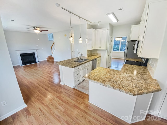 kitchen featuring light wood-type flooring, a sink, a peninsula, a fireplace, and dishwasher