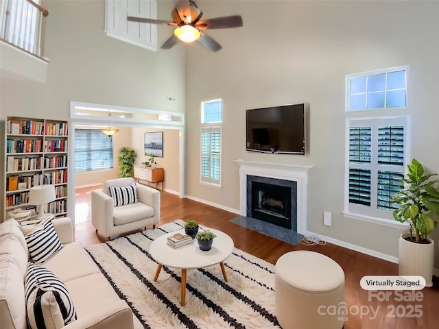 living area featuring a towering ceiling, plenty of natural light, wood finished floors, and a high end fireplace