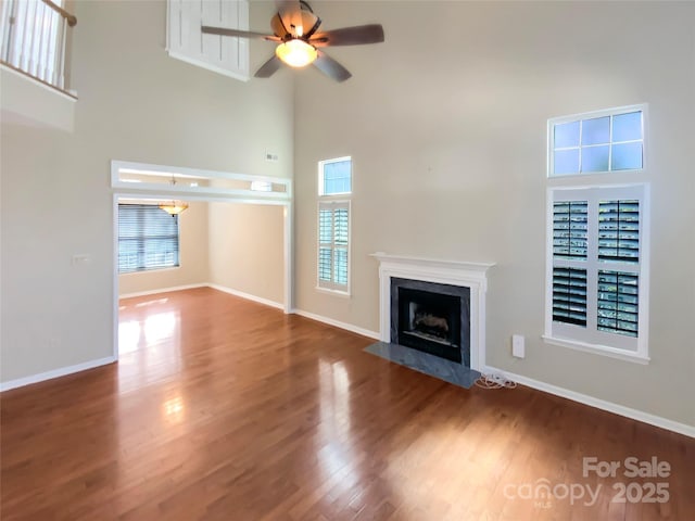 unfurnished living room with a wealth of natural light, a fireplace, a high ceiling, and wood finished floors