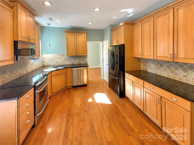 kitchen with light wood-type flooring, a sink, appliances with stainless steel finishes, decorative backsplash, and hanging light fixtures