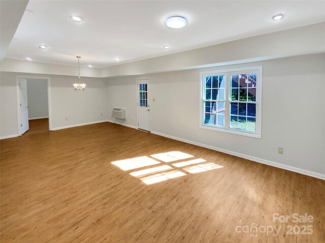 empty room with a notable chandelier, recessed lighting, baseboards, and wood finished floors