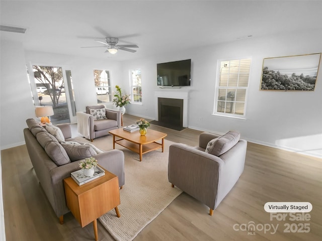 living area with light wood finished floors, visible vents, a ceiling fan, and a fireplace with flush hearth