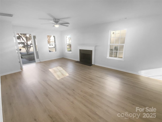 unfurnished living room with visible vents, a fireplace with flush hearth, baseboards, and wood finished floors