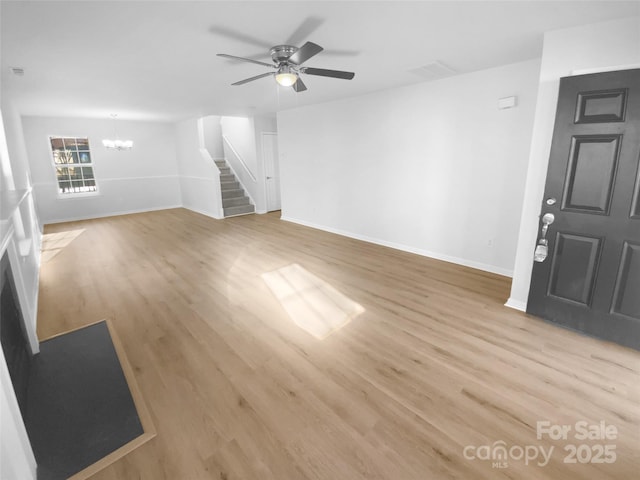 empty room with stairs, ceiling fan with notable chandelier, baseboards, and light wood finished floors