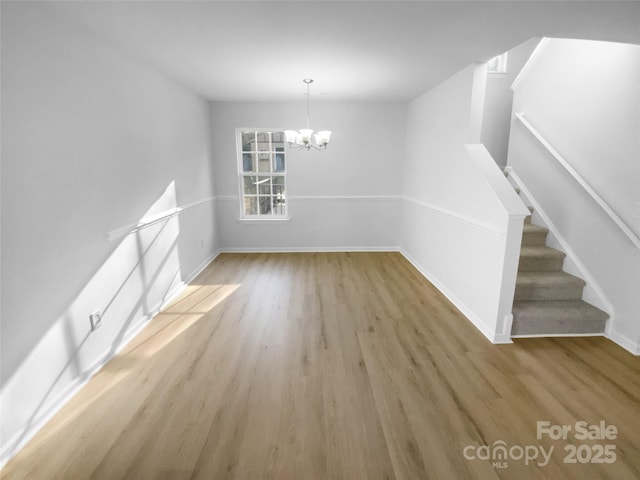 unfurnished dining area with stairway, baseboards, an inviting chandelier, and light wood-style flooring