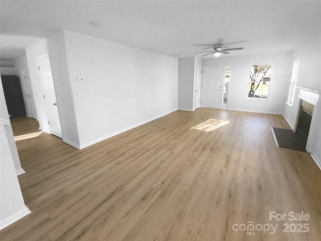 unfurnished living room featuring ceiling fan, baseboards, a fireplace with flush hearth, and light wood-style flooring