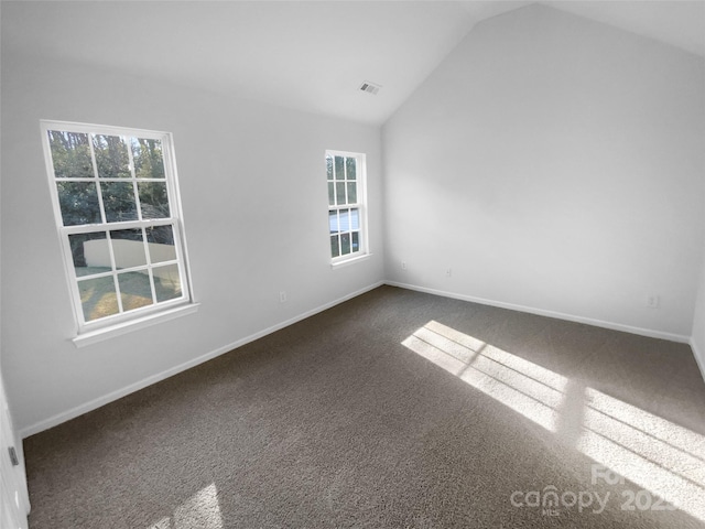 empty room featuring vaulted ceiling, visible vents, baseboards, and dark carpet