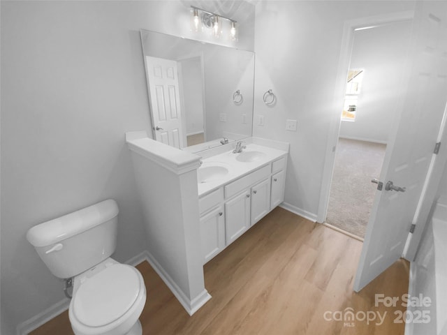 bathroom with baseboards, toilet, double vanity, wood finished floors, and a sink