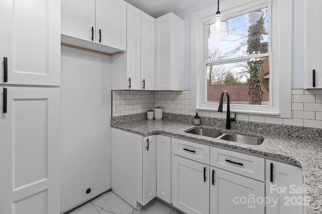 kitchen with marble finish floor, white cabinets, light stone countertops, and a sink