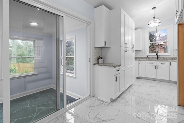 kitchen with white cabinets, light stone countertops, marble finish floor, and a wealth of natural light