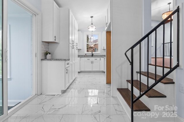 kitchen featuring a sink, marble finish floor, white cabinetry, tasteful backsplash, and a chandelier