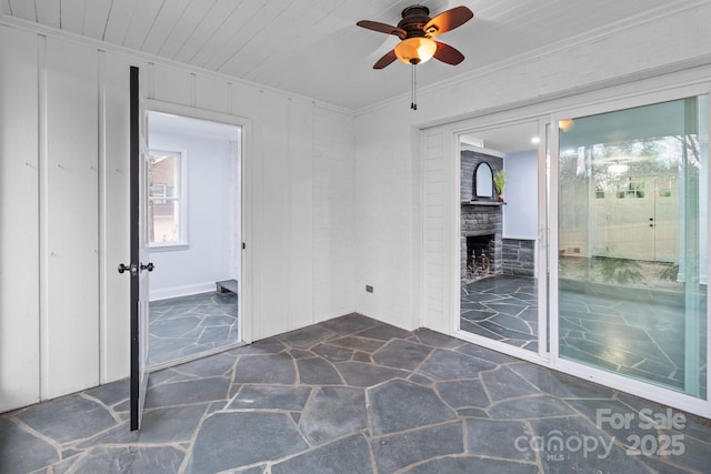 spare room featuring crown molding, stone flooring, wooden ceiling, a fireplace, and a ceiling fan