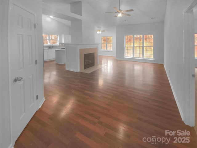 unfurnished living room with ceiling fan, baseboards, a tiled fireplace, vaulted ceiling, and wood finished floors