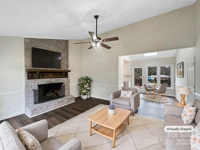 living area with lofted ceiling, wood finished floors, baseboards, a brick fireplace, and ceiling fan