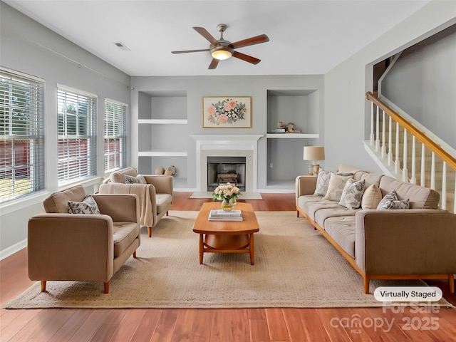 living area featuring a fireplace, built in features, wood finished floors, and visible vents