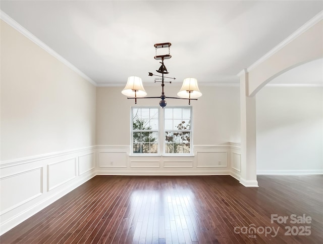 empty room featuring arched walkways, dark wood-style floors, crown molding, and a decorative wall