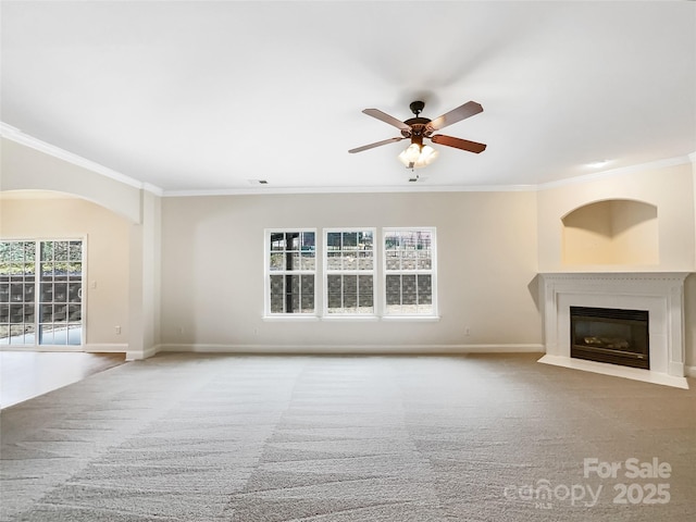 unfurnished living room with a ceiling fan, baseboards, carpet floors, a fireplace with flush hearth, and ornamental molding