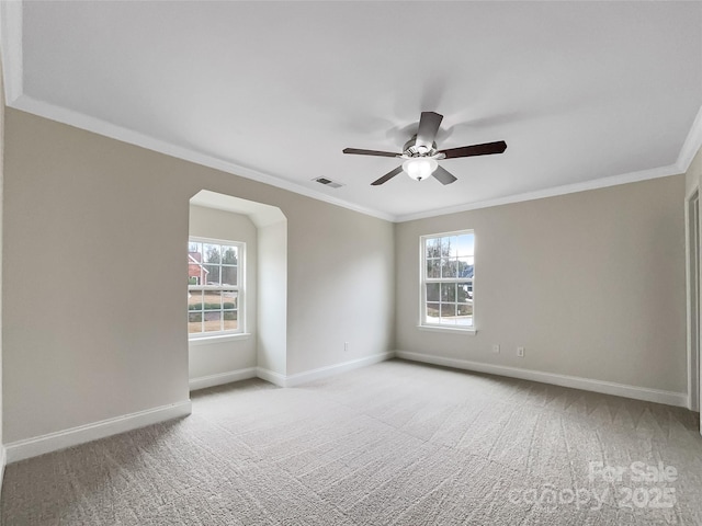 empty room with a wealth of natural light, visible vents, light colored carpet, and crown molding