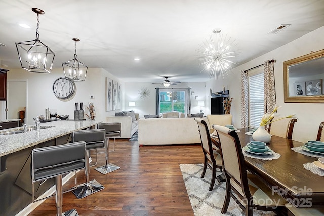 dining area featuring visible vents, ceiling fan with notable chandelier, and dark wood-type flooring