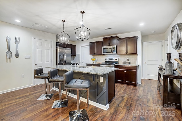 kitchen featuring tasteful backsplash, dark brown cabinetry, a breakfast bar, dark wood-style floors, and stainless steel appliances